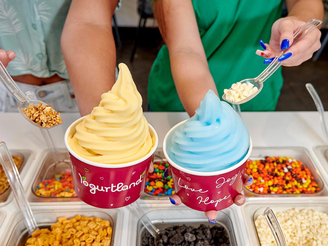 Two Yogurtland frozen yogurt cups with an assortment of toppings